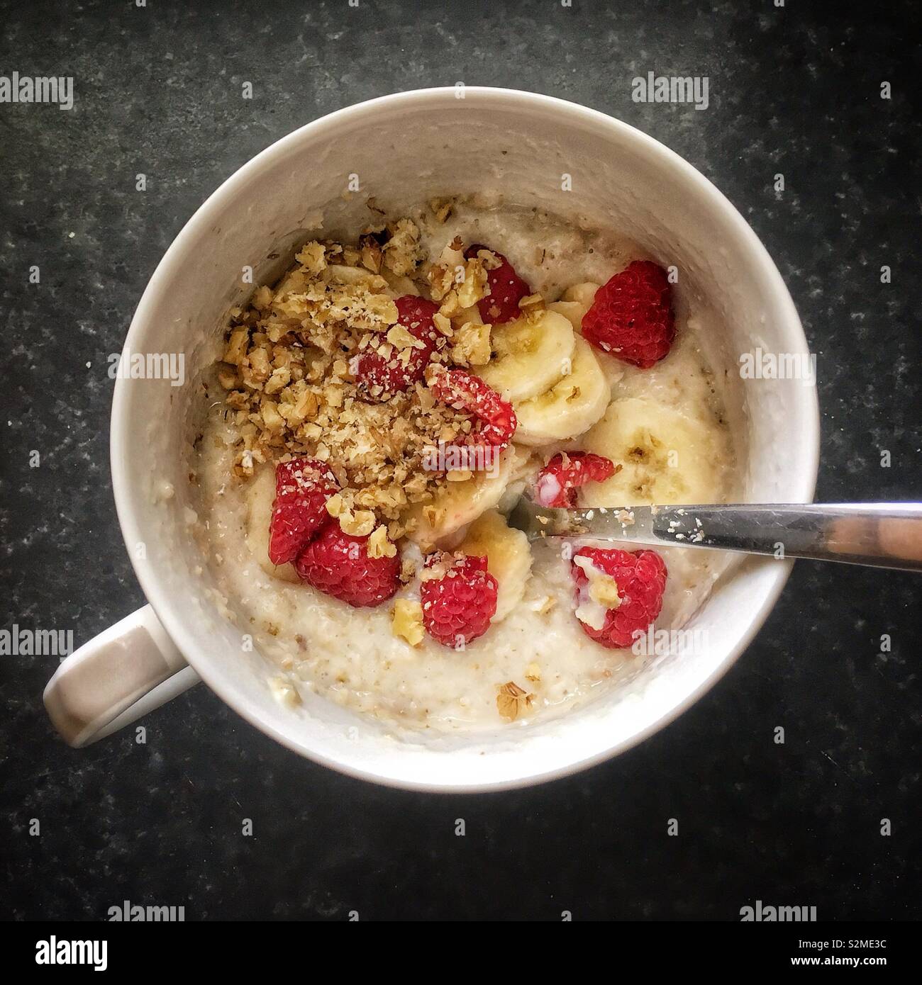 Brei in eine Porzellanschüssel mit Bananen, Himbeeren und zerkleinerte Walnüsse. - Smartphone-aufgenommenes Stockfoto