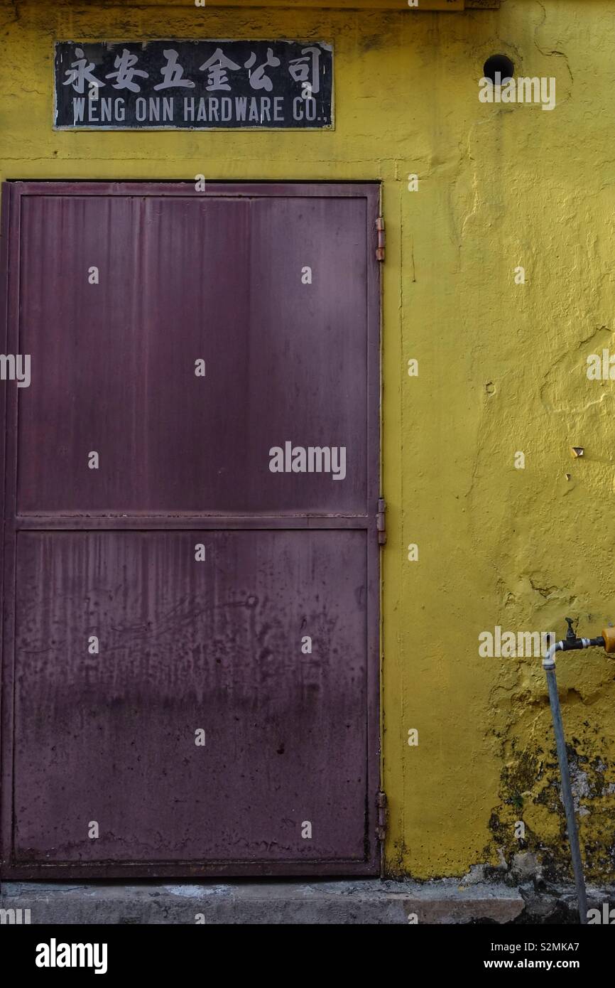 Hinterhof. Backdoor zu einem Geschäft. Braun und Rusty im Gegensatz zu einem hellen gelben wand. Chinesischen Buchstaben an die Wand und sprach "hardware Trading". Stockfoto