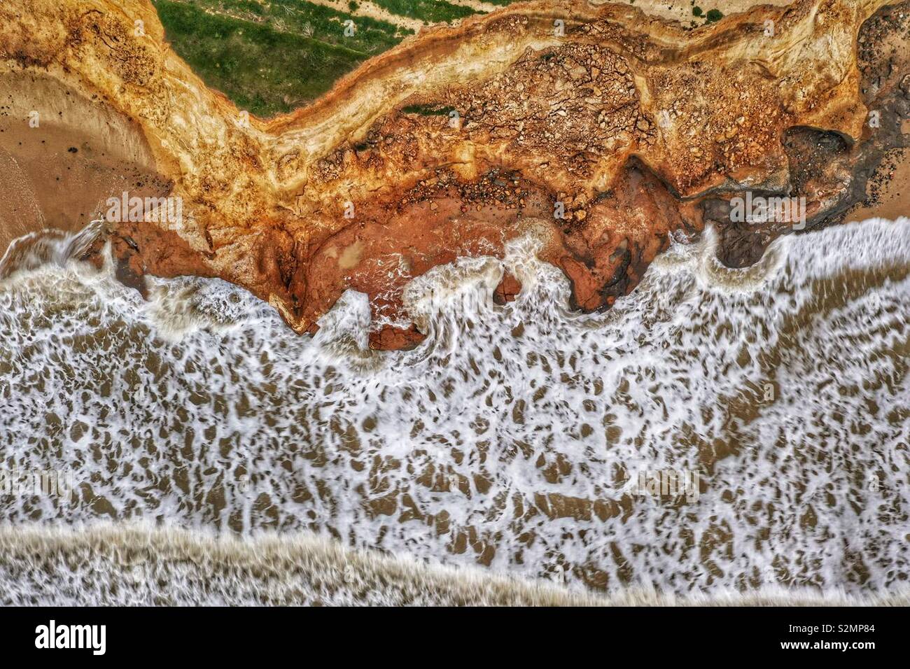 Von oben nach unten Luftbild der Wellen, die gegen eine Klippe mit einem interessanten Muster brechen - Smartphone-aufgenommenes Stockfoto
