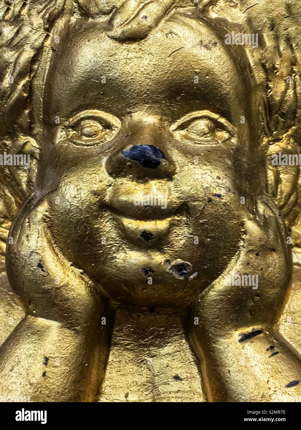 Nahaufnahme einer Glücklich lächelnde Gold bemalt Gesicht eines Jungen cherub Statue. - Smartphone-aufgenommenes Stockfoto