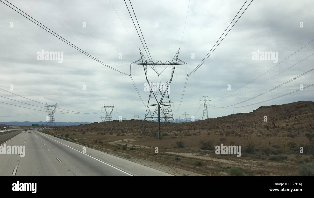 Zeilen von Masten Lager hohe Spannung elektrische Leitungen Kreuzung Freeway und verschwand in Richtung Berge, Apple Valley Region, Kalifornien. Bewölkter Tag Stockfoto