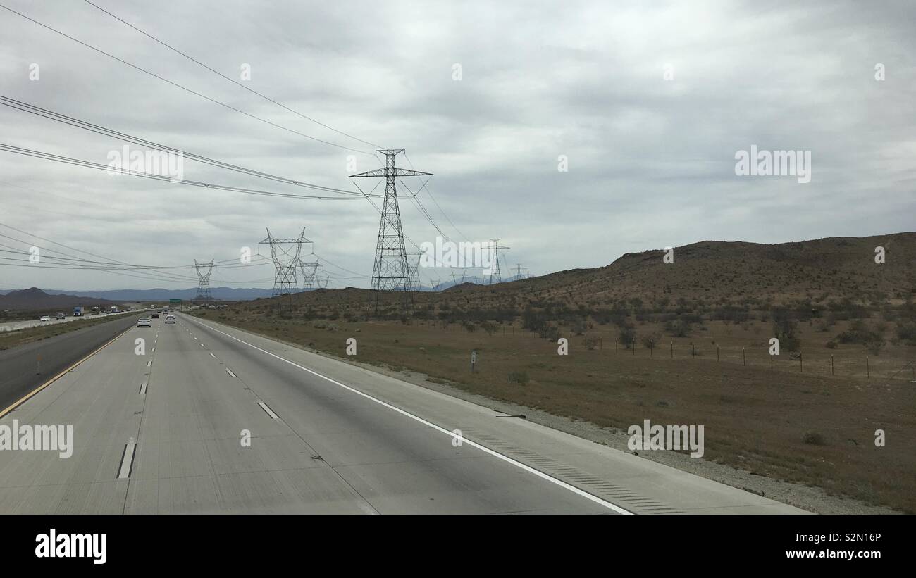 Freeway mit Strommasten und hohe Spannung elektrische Leitungen Kreuzung in bergigen, Apple Valley Region Kalifornien. Bewölkter Tag Stockfoto