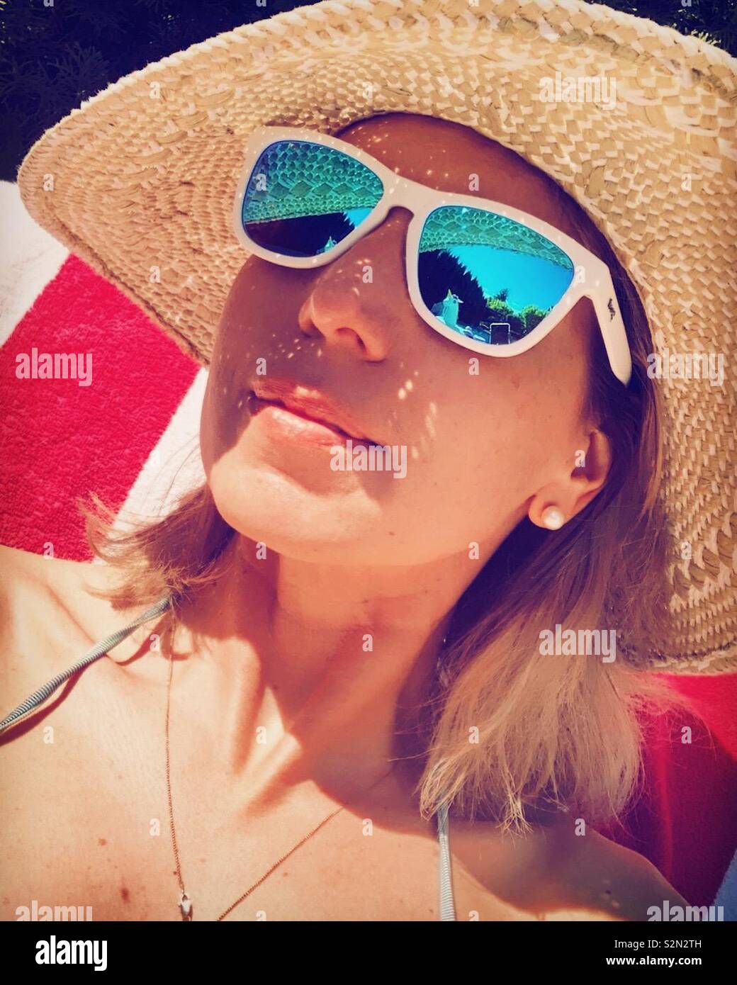 Frau mit Sonnenbrille und einen Strohhut an einem sonnigen Tag. - Smartphone-aufgenommenes Stockfoto