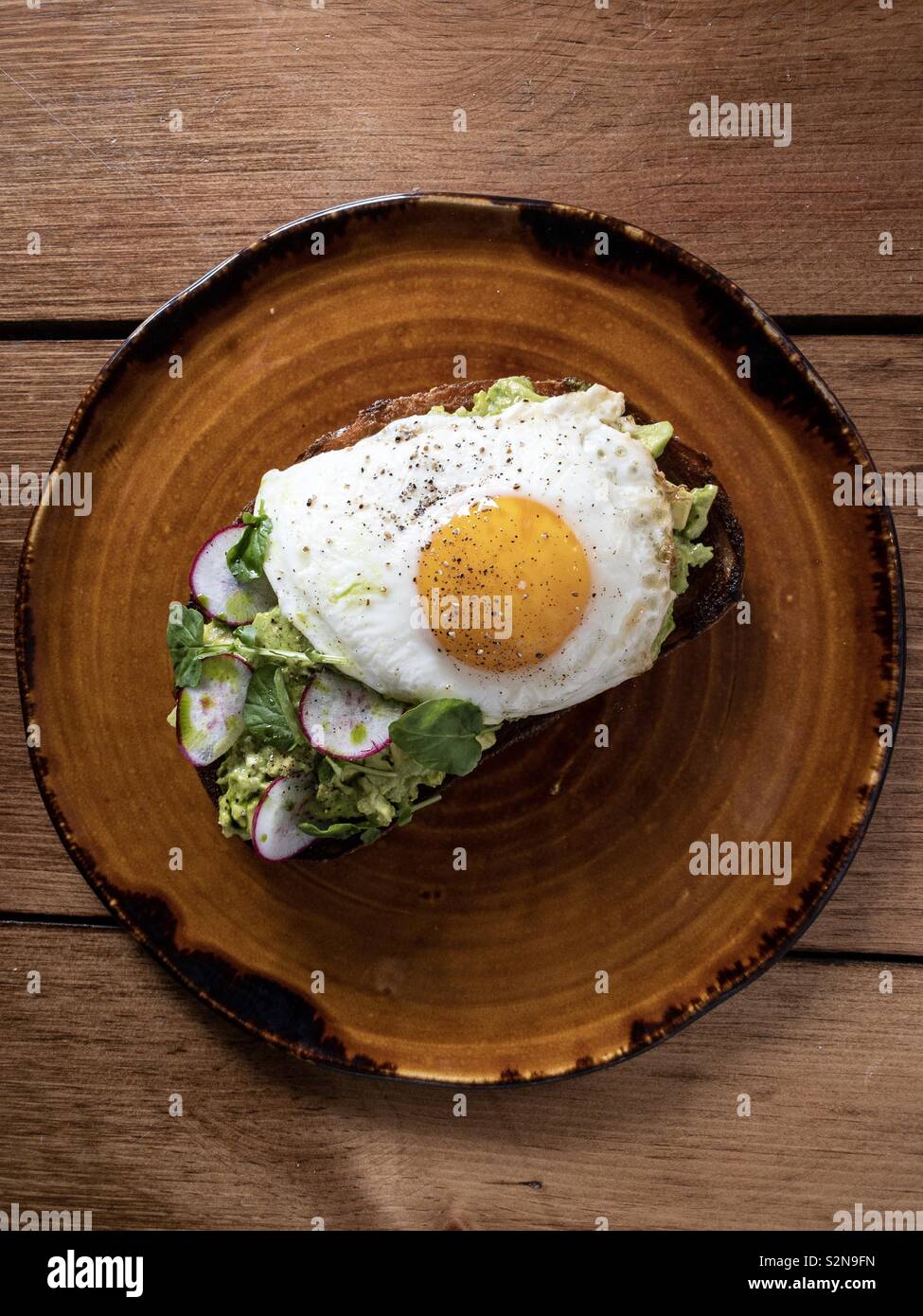Avocado Toast mit sunny side up Ei auf braun Teller zum Frühstück Stockfoto