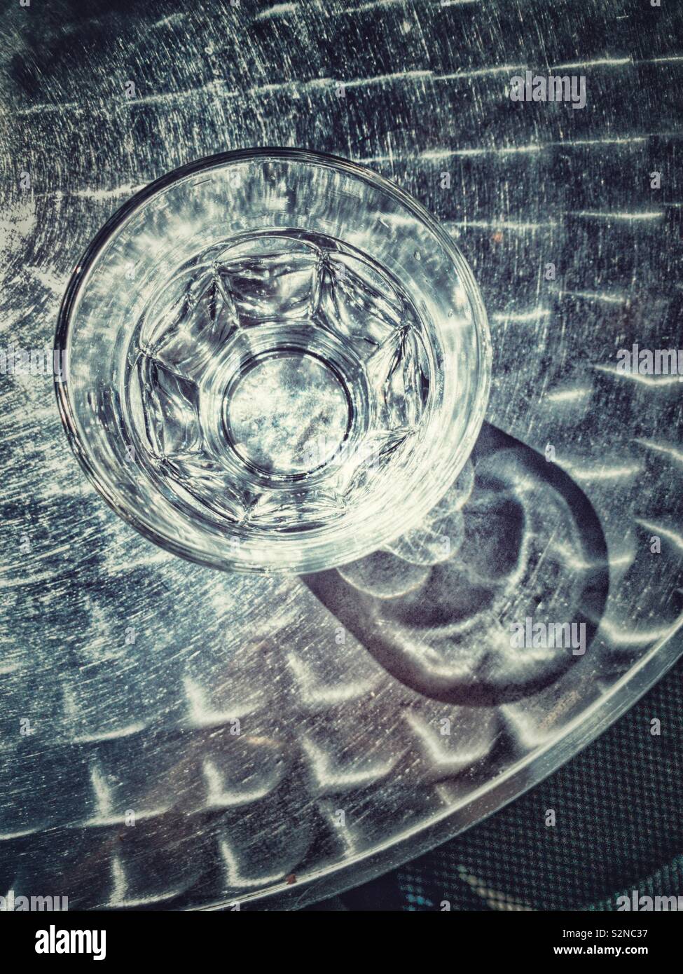 Wasser im Glas auf Metall Tisch, draußen mit harten Schatten von hellem Sonnenlicht. Stockfoto