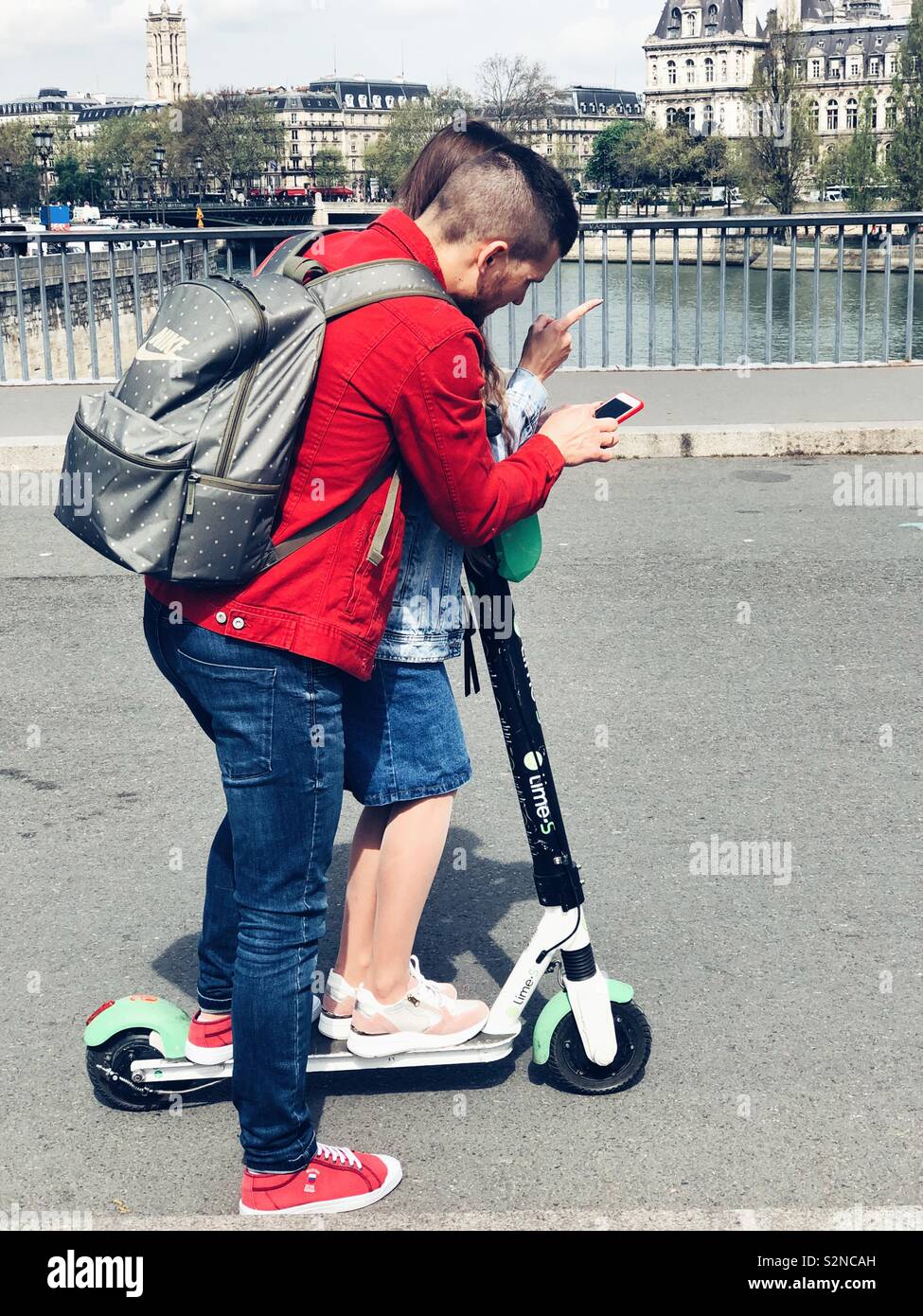 Junge modische Paar versuchen, eine elektrische Kalk scooter auf einer Brücke in Paris, Abbildung Stockfoto