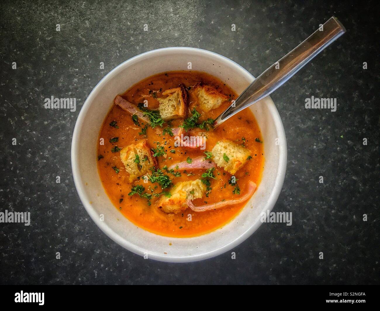 Eine Schüssel mit Karotte und Koriander Suppe mit Croutons, Speck und Petersilie. Stockfoto