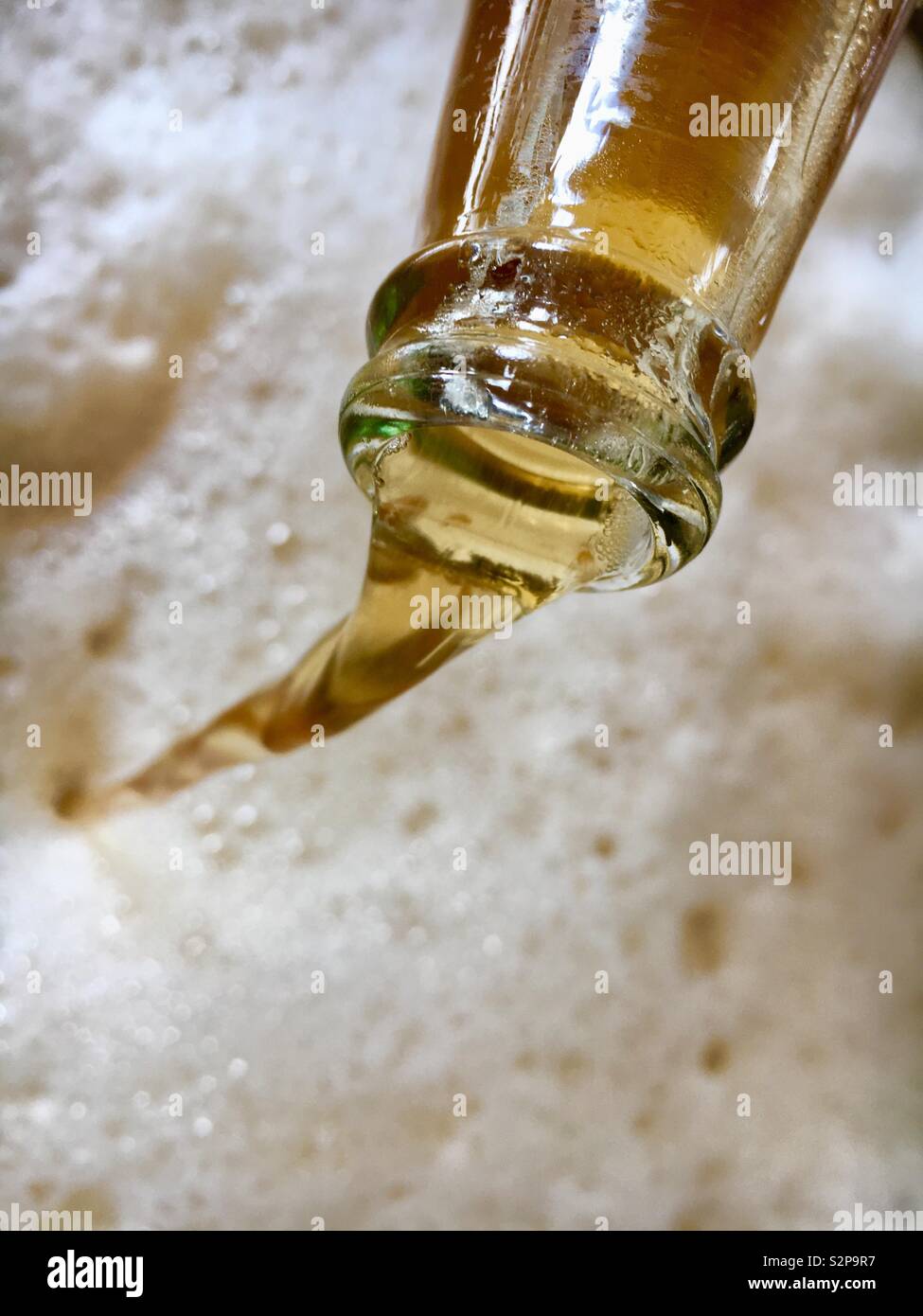 Lagerbier aus einem Glas Flasche ausgegossen und verursachen ein schaumiges Bier Schaum zu bilden Stockfoto