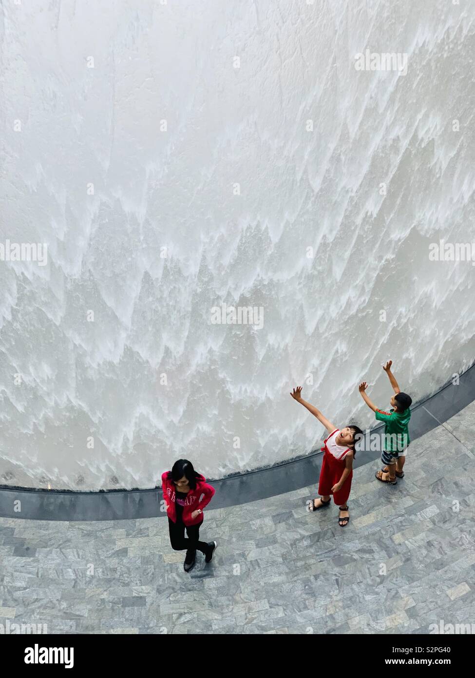 Posing Frau und zwei Kinder vor Wasserfall bei Juwel in Changi Airport Singapur - Smartphone-aufgenommenes Stockfoto