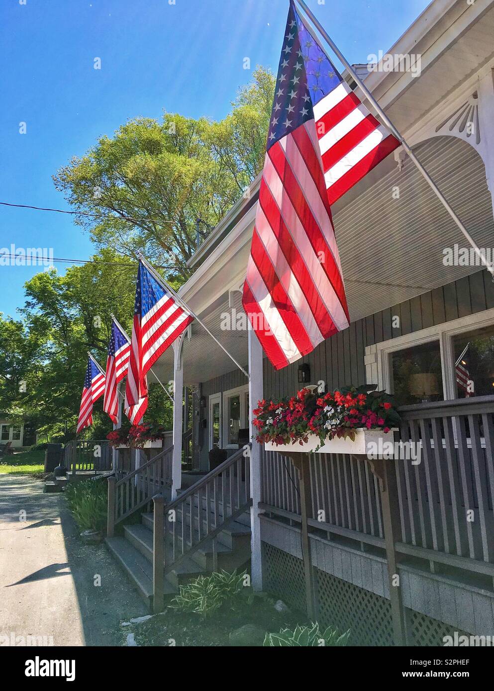 Mehrere amerikanische Fahnen wehen patriotisch auf der Veranda eines Storefront auf sonnigen Sommertag mit blauer Himmel in Egg Harbor WI - Smartphone-aufgenommenes Stockfoto