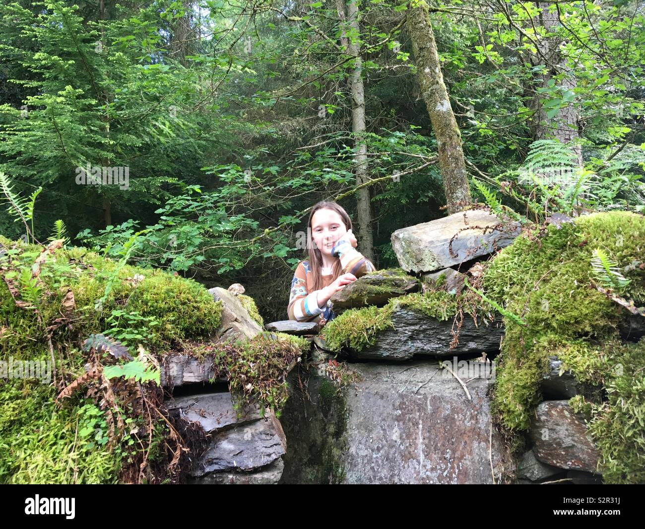 Mädchen steht hinter der Wand zuwachsen mit Moos im Wald Stockfoto