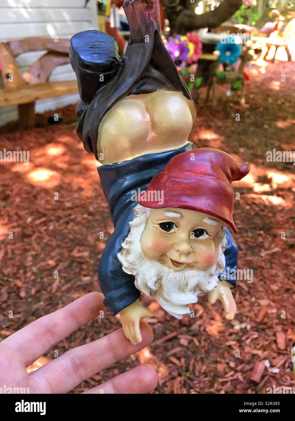 Hanging Garden gnome Statue mit blauen Shirt rote Mütze und weißem Bart mit freiliegenden Gesäß Hand in Hand mit einem menschlichen Stockfoto