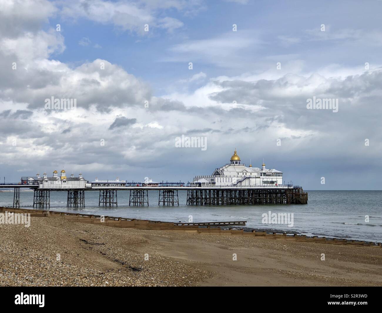 Eastbourne Pier, East Sussex, Großbritannien bei Ebbe am Strand an einem Frühlingstag mit Sturmwolken in der Ferne. - Smartphone-aufgenommenes Stockfoto