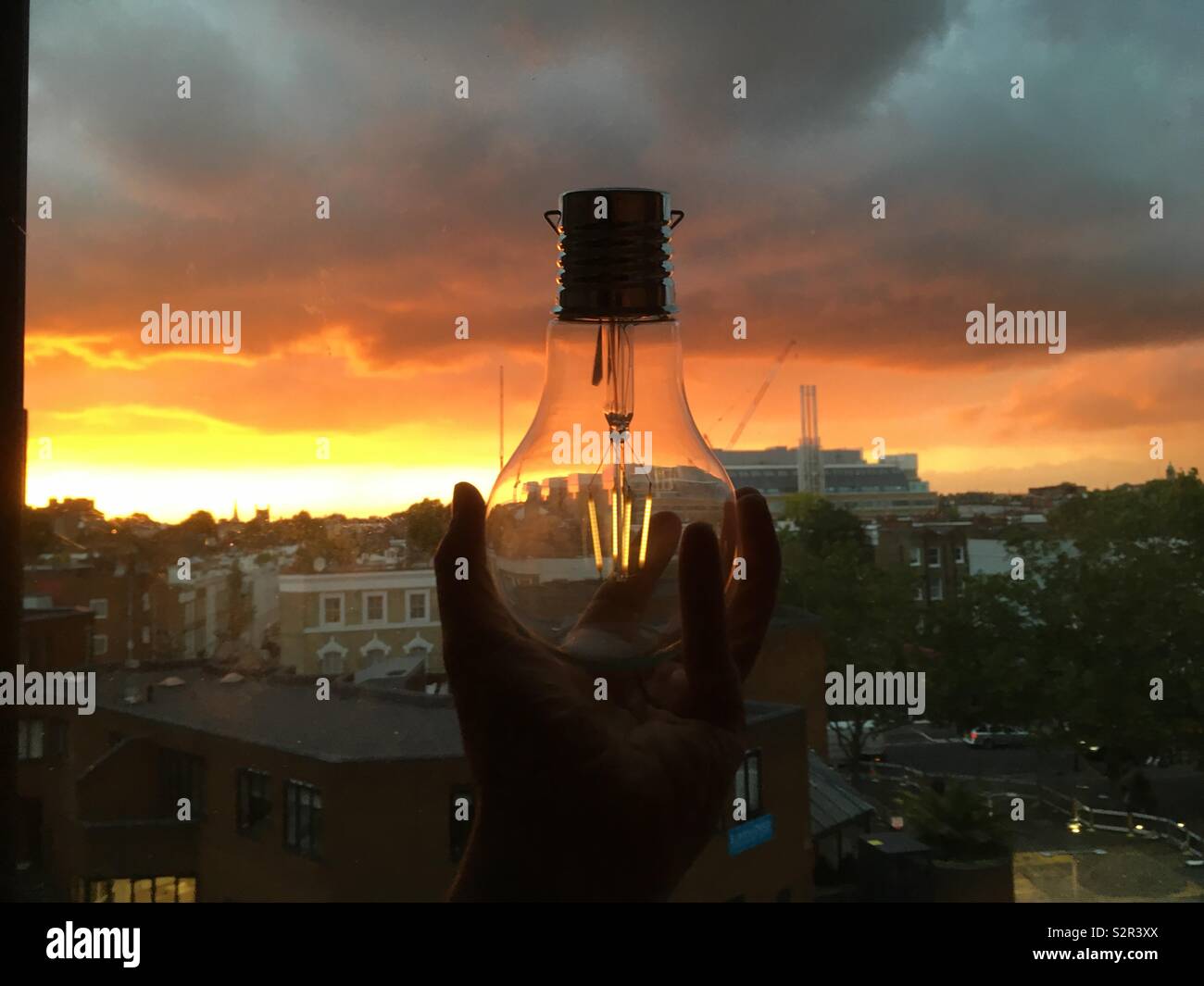 Hand mit Solar Lampe gegen den Hintergrund der Sonnenuntergang und Approaching Storm. - Smartphone-aufgenommenes Stockfoto
