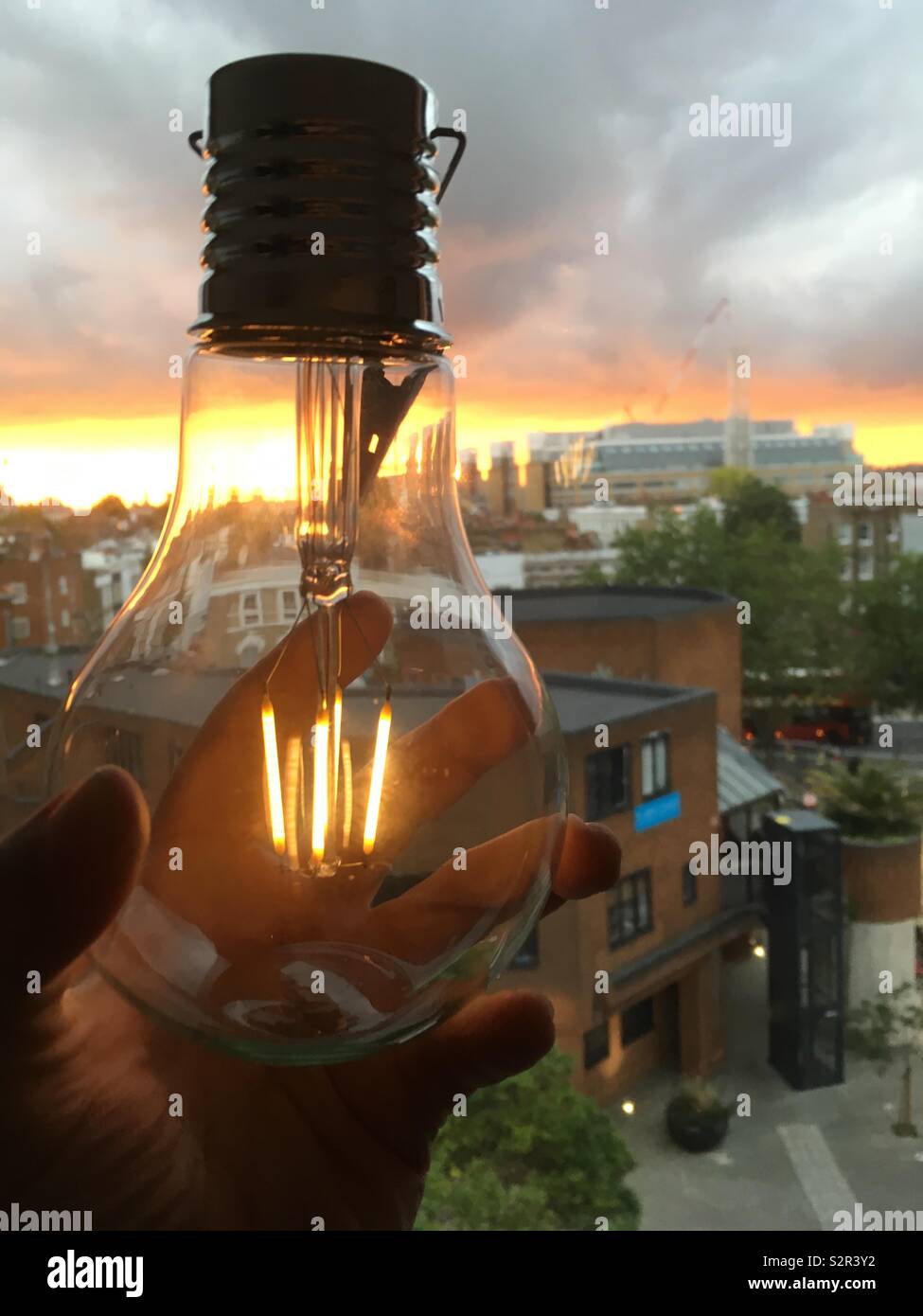 Hand Halten eines Solar Lampe gegen den Hintergrund der Sonnenuntergang und Approaching Storm clouds. - Smartphone-aufgenommenes Stockfoto