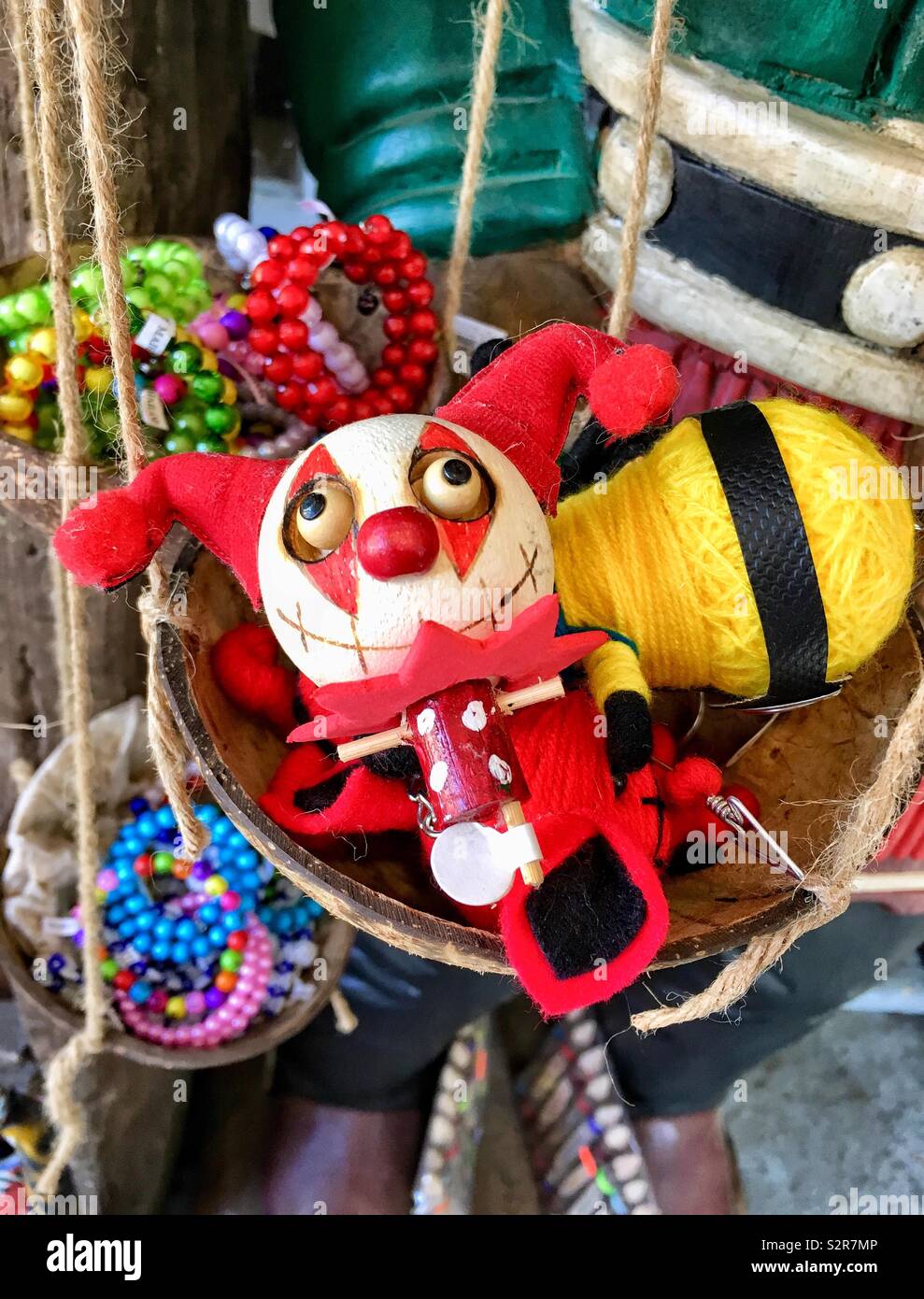 Holz- pin jester Puppe neben einem handgefertigten Minion Puppe von gelben Garn in einer Kokosnuss, die von bunten Perlen Armbänder umgeben sind Stockfoto