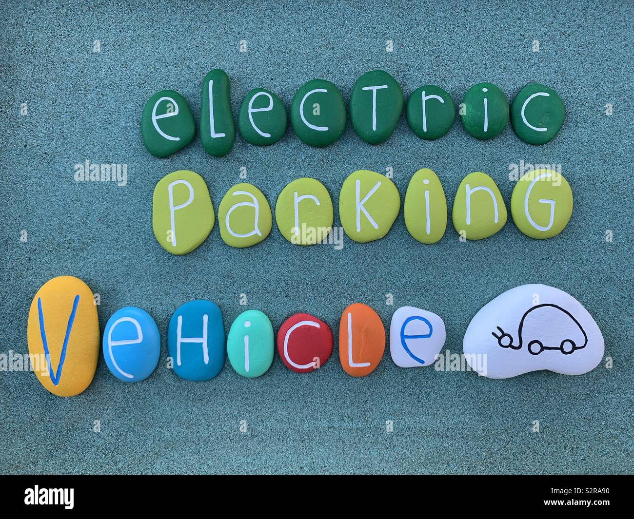 Elektrische Fahrzeug parken, konzeptionelle Logo Art Steine Zusammensetzung über grünen Sand - Smartphone-aufgenommenes Stockfoto