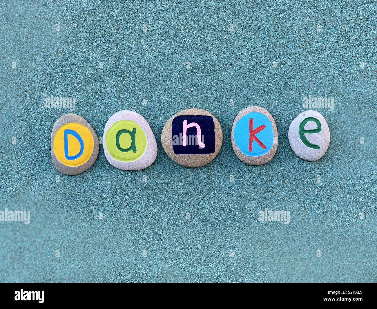Danke, vielen Dank, dass Sie sich in deutscher Sprache verfasst, mit farbigen Steine über grünen Sand Stockfoto