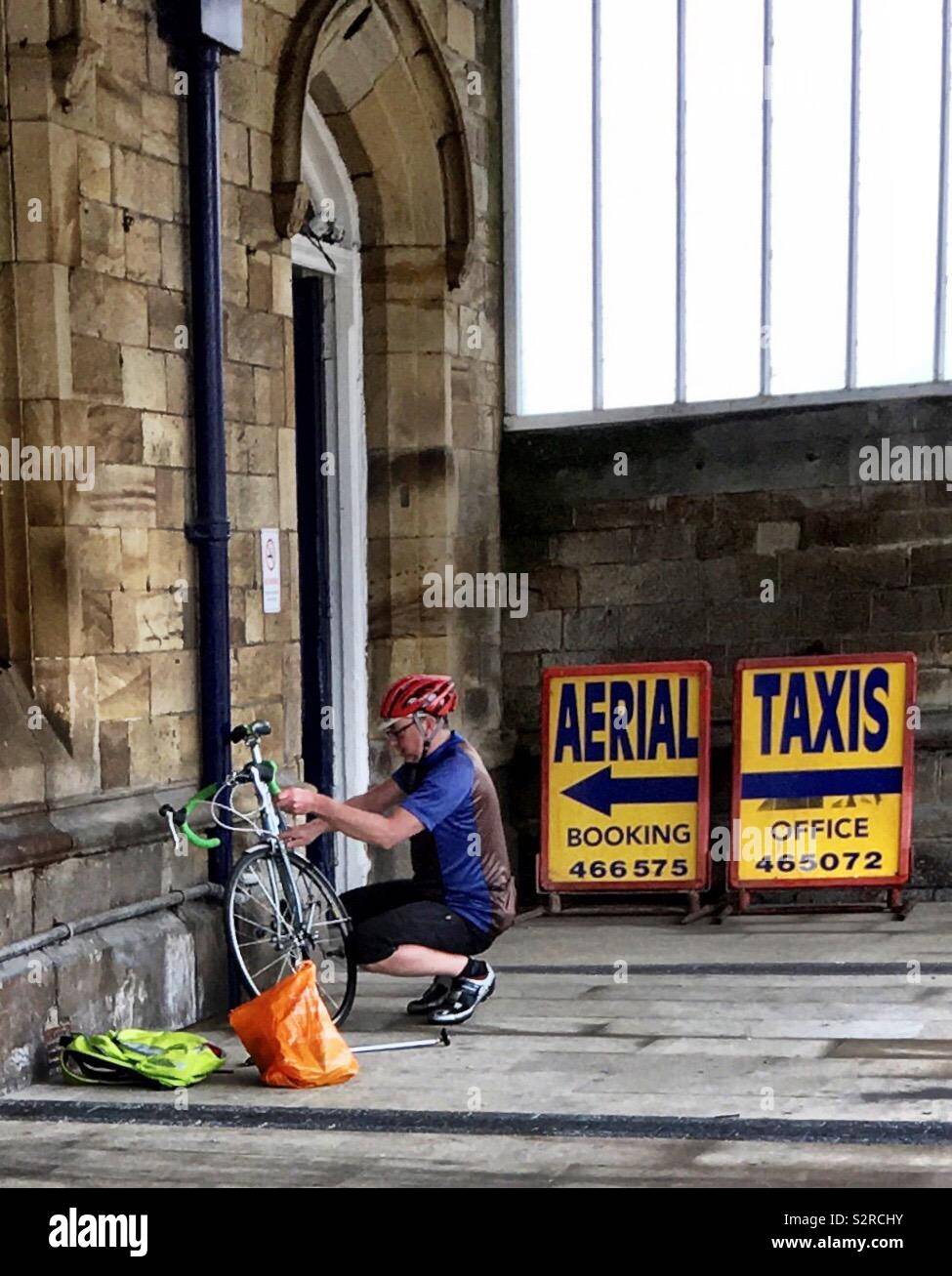 Männliche Radfahrer Reparatur Fahrrad gegen historischen Bahnhof Mauer in Dewsbury, West Yorkshire, UK. 26 Juni, 2019. Stockfoto