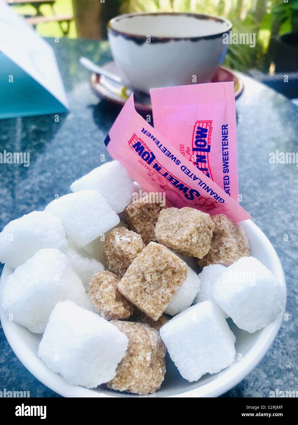 Schüssel aus weißem und braunem Zucker Würfel mit Beutel von Süßstoff auf einem Tisch im Freien Stockfoto