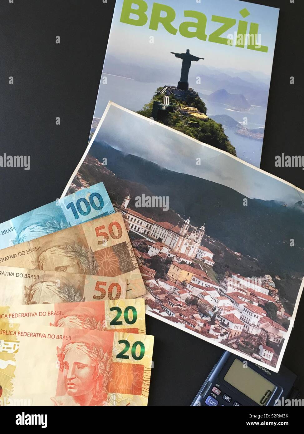 Die Vorbereitung für eine Reise nach Brasilien, brasilianische Real (Währung), einen Rechner, eine Postkarte von Ouro Preto in Minas Gerais, und einige touristische Informationen über Brasilien. Stockfoto