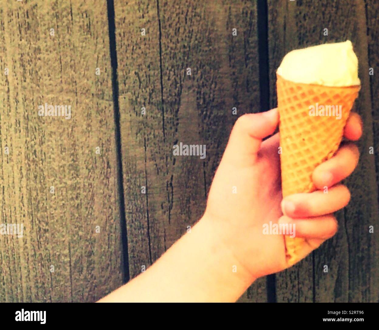 Ein Junge mit einem Vanille Eis in der Hand durch einen Holzzaun an einem Sommertag. USA, Nordamerika Stockfoto