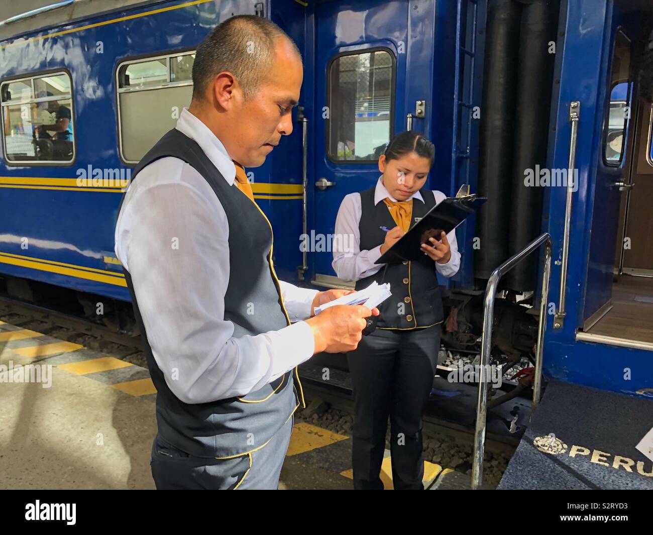 Zwei 2 Perurail Beamte vom Bahnhof in Aguas Calientes (Machu Picchu Machu Picchu Pueblo), dem Mann die Kontrolle der Flugscheine und der Frau weibliche Schreiben auf eine Zwischenablage. Stockfoto