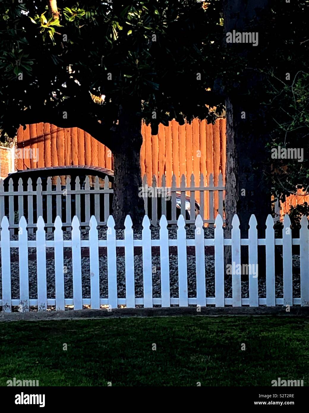 Einen ruhigen Abend Sonnenuntergang spiegelt auf einem Zaun hinter einer weißen Lattenzaun. Dies ist suburbanen Lebens von seiner besten Seite. Stockfoto
