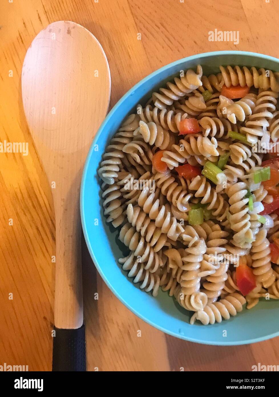 Ein leckeres Schüssel Nudelsalat mit Paprika, Karotten und Gurken auf einem Holztisch serviert mit einem Holzlöffel. Stockfoto