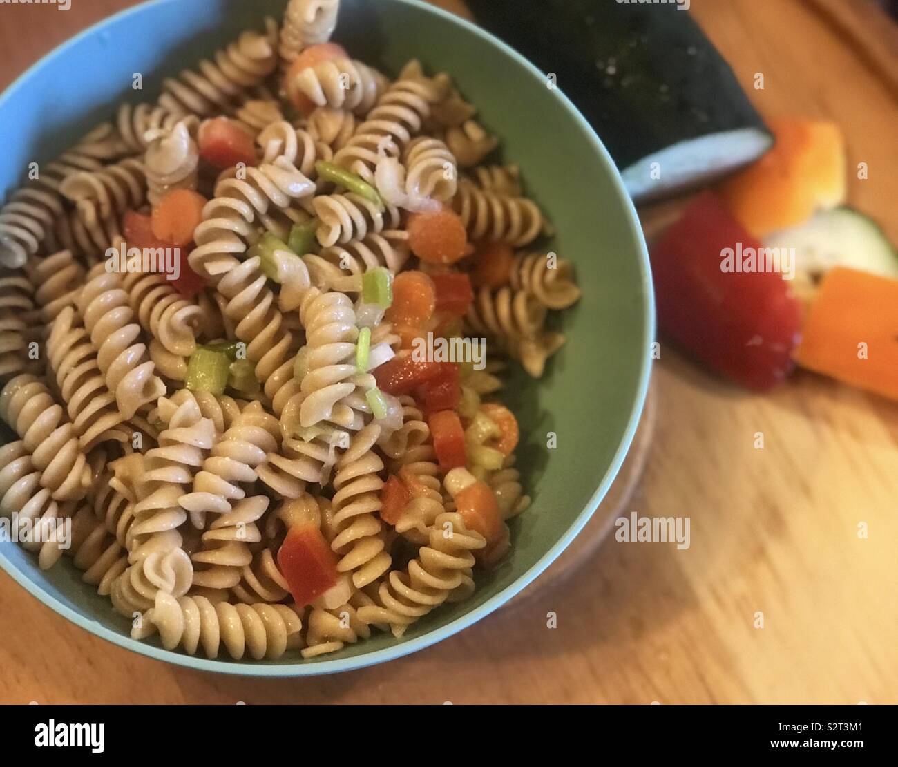 Eine köstliche Schüssel Nudelsalat mit Paprika, Gurken, Knoblauch würzen und Karotten, mit gehacktem Gemüse auf der Seite angezeigt. Stockfoto