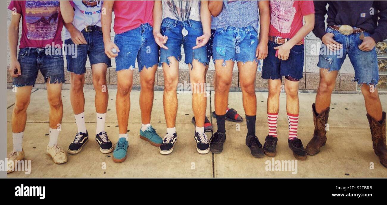 Sieben jungen aufgereiht in einer Reihe tragen bunte Kleidung, Cutoff jean Shorts, Cowboy Stiefel und Turnschuhe Stockfoto