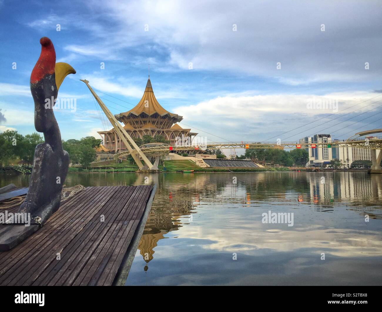 Der Bug eines traditionellen malaysischen Iban longboat, da es Ansätze der Darul Hana Brücke über den Fluss Sarawak und der Staatlichen Legislative Assembly Building, Kuching, Sarawak, Malaysia Stockfoto