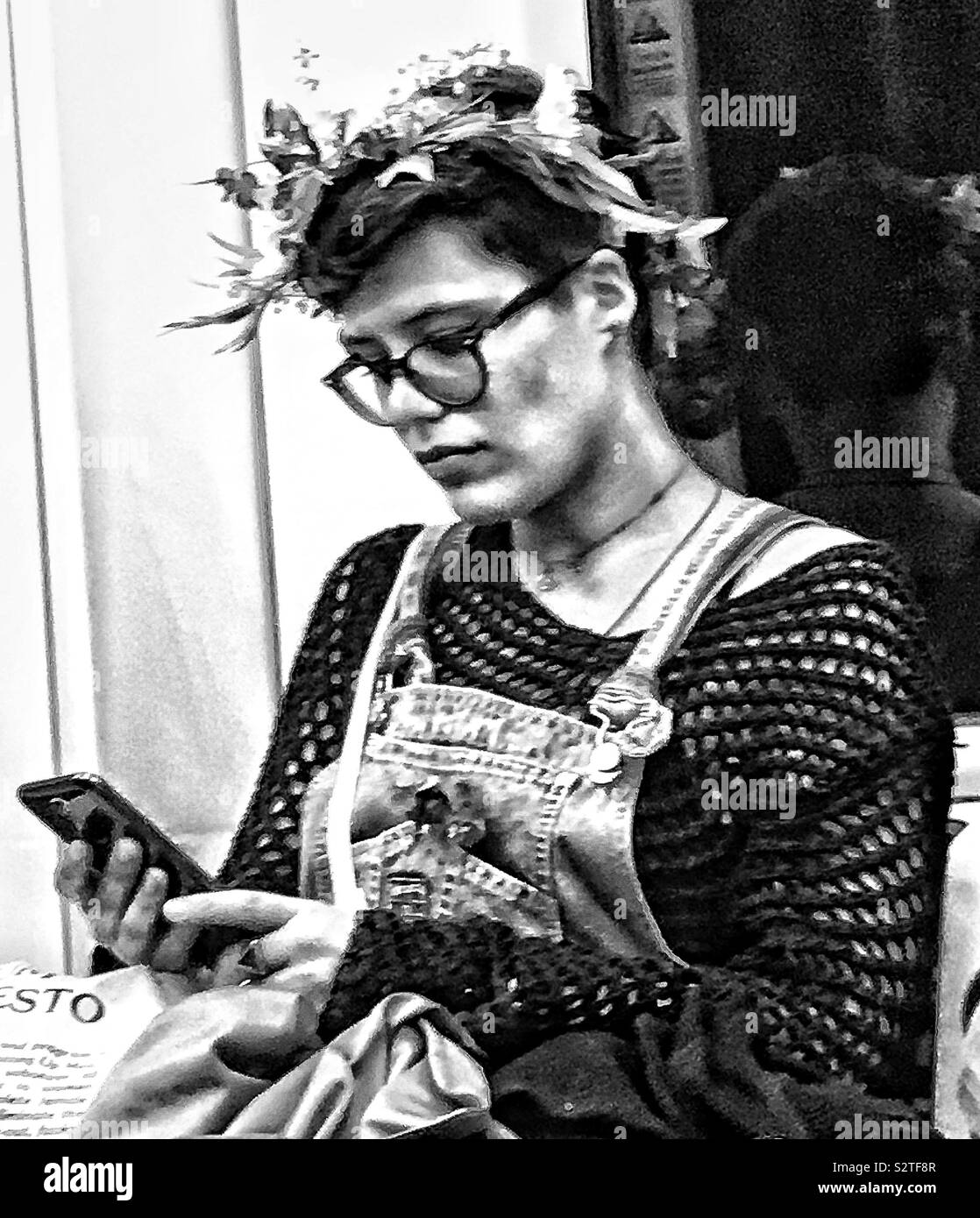 Junge bebrillte Dame auf einem Zug auf ihr Mobiltelefon. Ihr Aussehen ist eher unkonventionell. Das Portrait ist in Schwarz und Weiß. Stockfoto