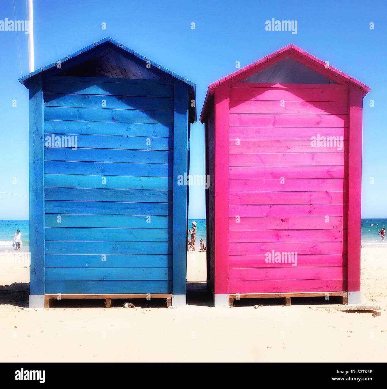 Zwei bunten Holzhütten an einem Sandstrand, ein Licht blau, die anderen rosa, eingesetzt als Umkleidekabinen. Stockfoto