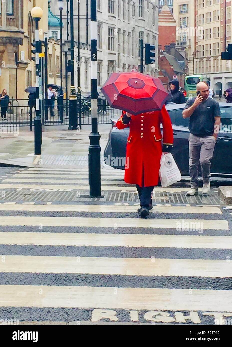 Einem Beefeater trägt einen roten Regenschirm auf einem nassen Tag in London, London, Großbritannien - Smartphone-aufgenommenes Stockfoto