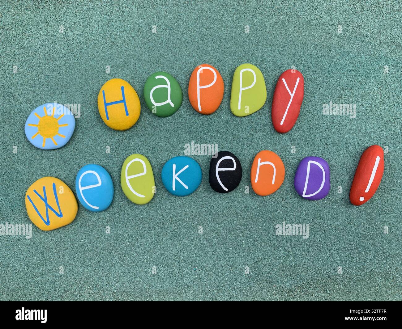 Happy Weekend Text mit farbigen Steinen über grünen Sand Stockfoto