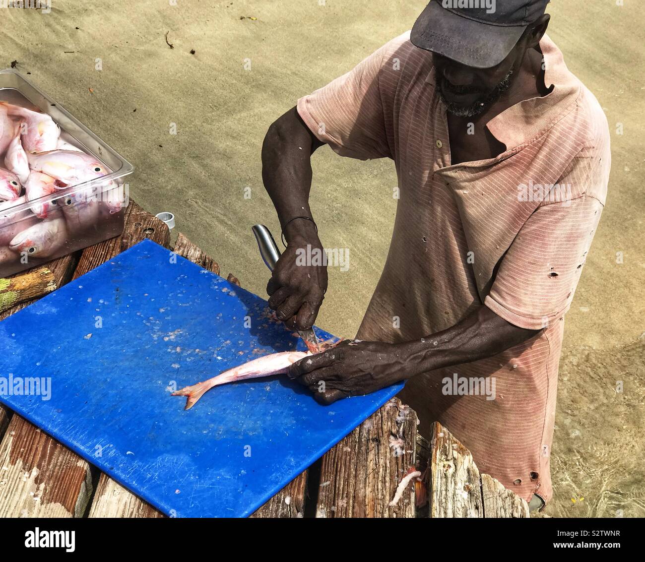 Man ausnehmen Fische am Steg mit den Füßen im Wasser, Prinzessin Margaret Strand, Bequia, St. Vincent und die Grenadinen - Smartphone-aufgenommenes Stockfoto