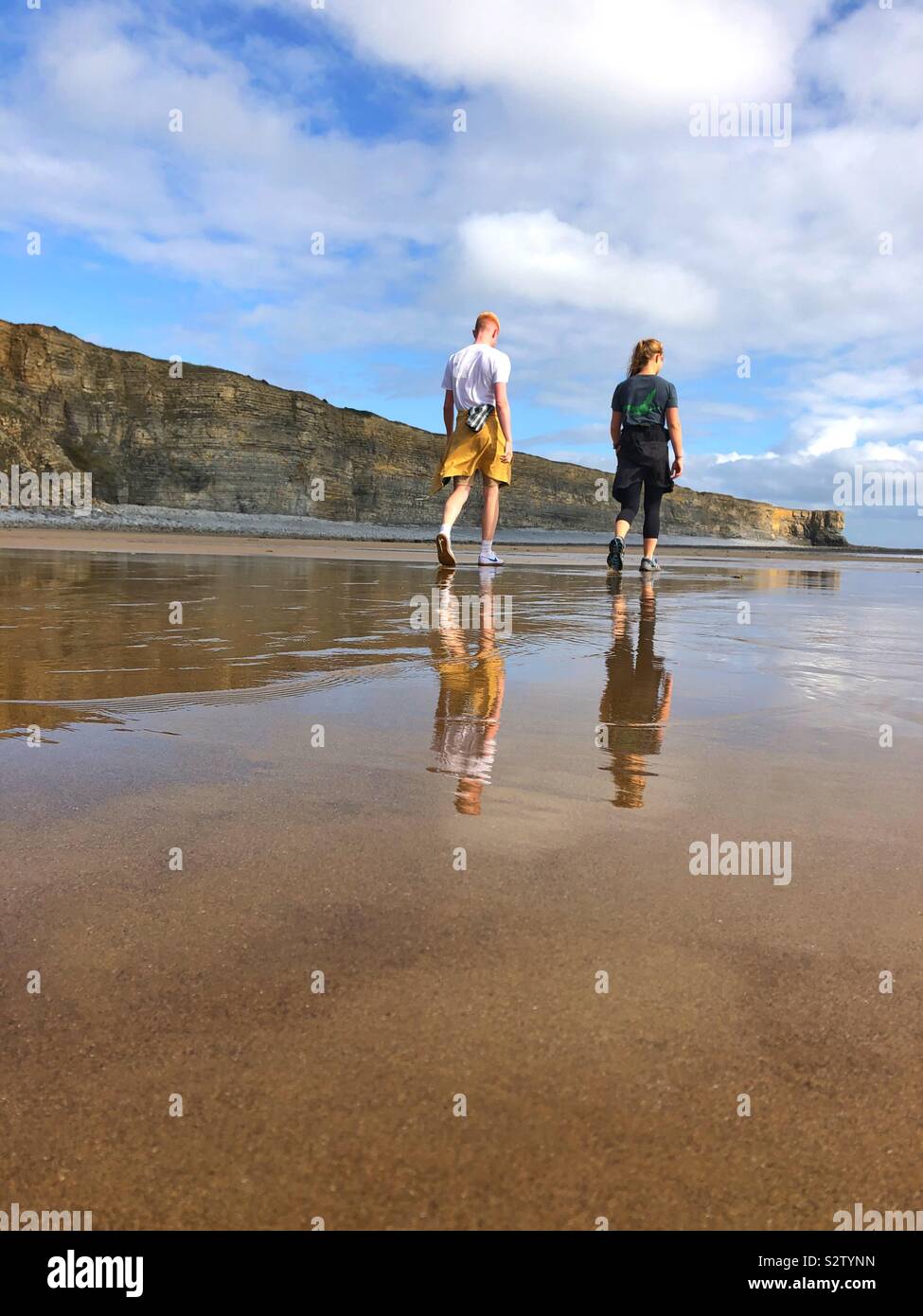 Zwei junge Menschen zu Fuß am Strand mit Reflexionen in den nassen Sand, Wales. Stockfoto