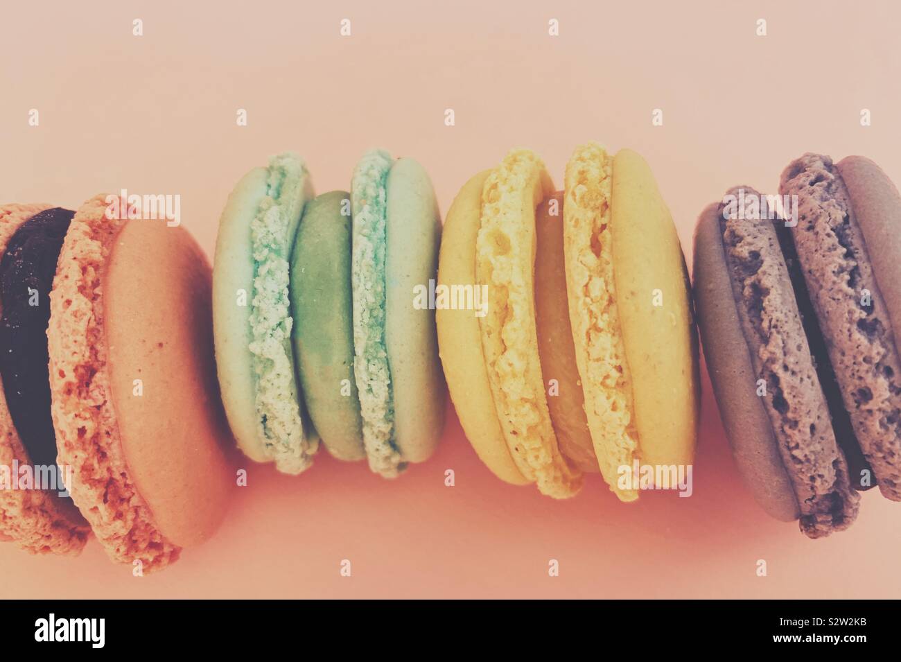 Bunte, frische, pastellfarbene Macarons Reihen sich an und werden von oben mit rosa Hintergrund fotografiert. Stockfoto