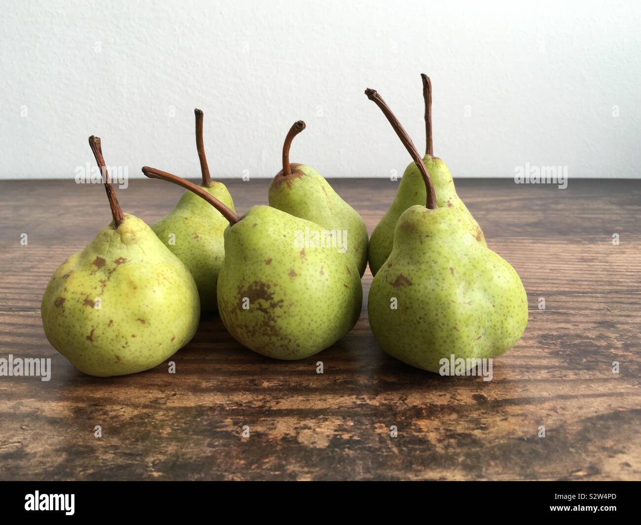 Birnen auf einem hölzernen Tisch gegen eine weiße Wand Hintergrund - Smartphone-aufgenommenes Stockfoto