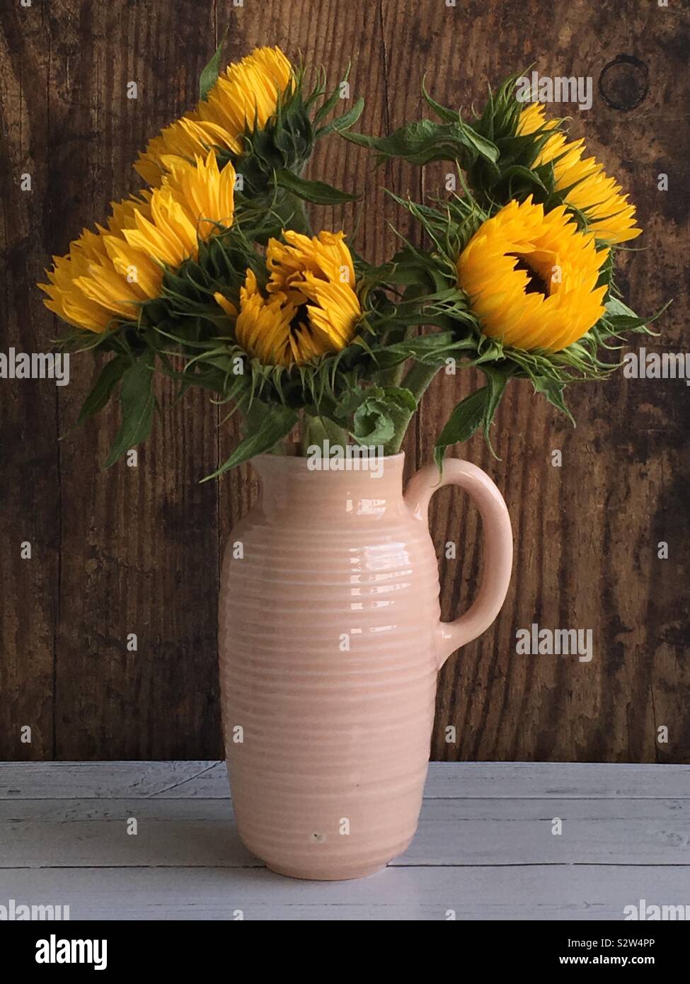 Ein rosa Vase auf weißem Holz Tisch gegen eine hölzerne Verkleidung Hintergrund - Smartphone-aufgenommenes Stockfoto