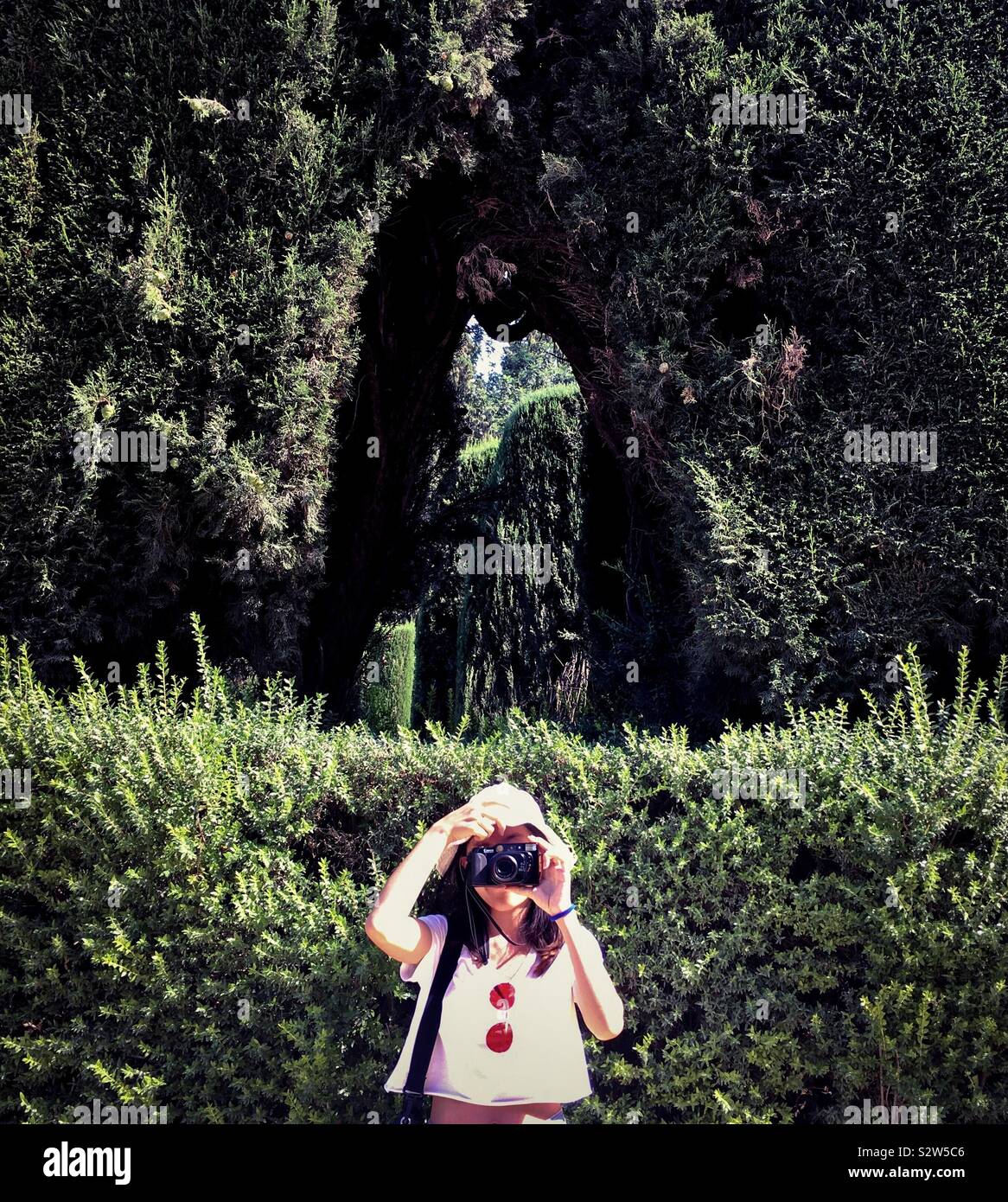 Vorderansicht des Mädchens unter Foto mit der Kamera vor einem Garten Stockfoto