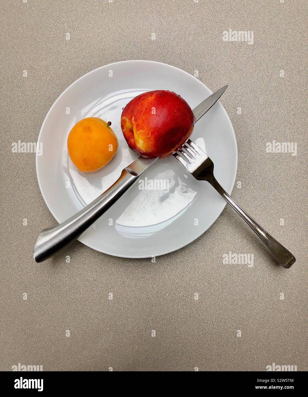 Ein weißer Teller mit Obst mit Messer und Gabel vorbereitet. - Smartphone-aufgenommenes Stockfoto