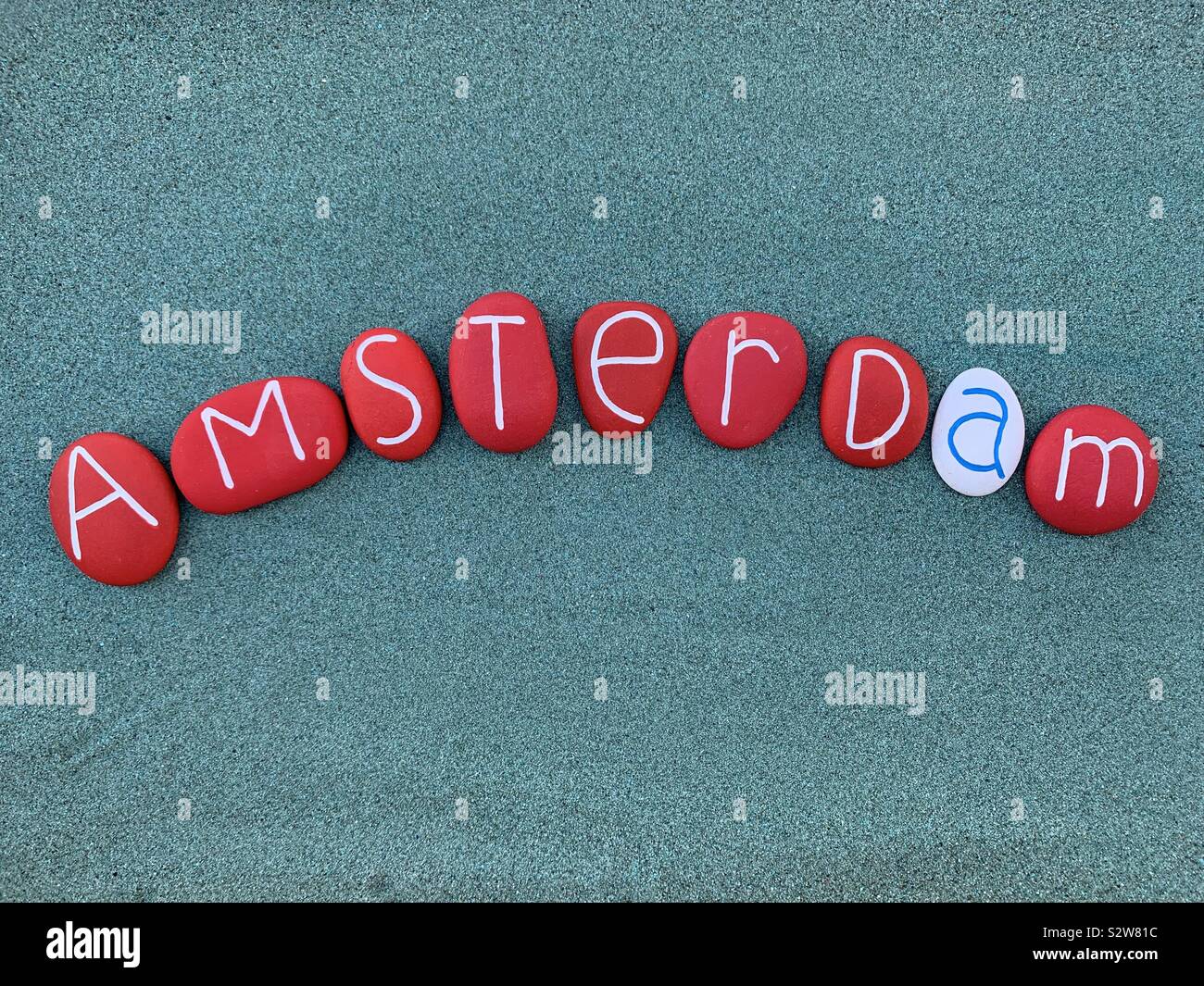 Amsterdam, kreative logo und Souvenir Idee komponiert mit geschnitzten und bemalten Steinen über grünen Sand - Smartphone-aufgenommenes Stockfoto