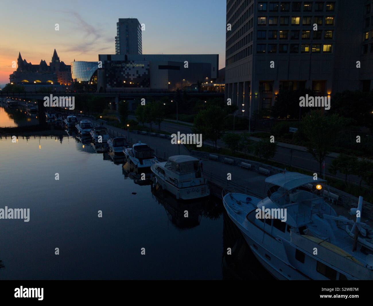 Die Boote in der Rideau Canal, der Innenstadt von Ottawa, der Hauptstadt Kanadas, frühe Nacht, 18. August 2019. Das Chateau Laurier Silhouette ist weit weg gegen den Sonnenuntergang Himmel gesehen. Stockfoto