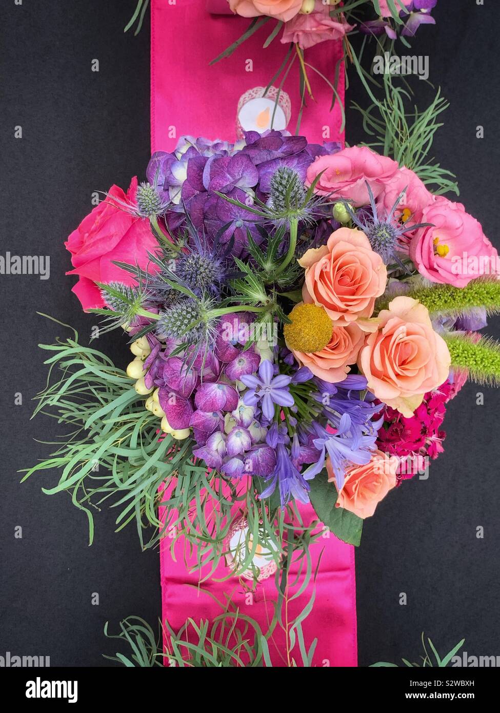Schöne Blume Anordnung mit dunkel rosa Rosen in voller Blüte auf einem schwarzen Tischdecke. Stockfoto