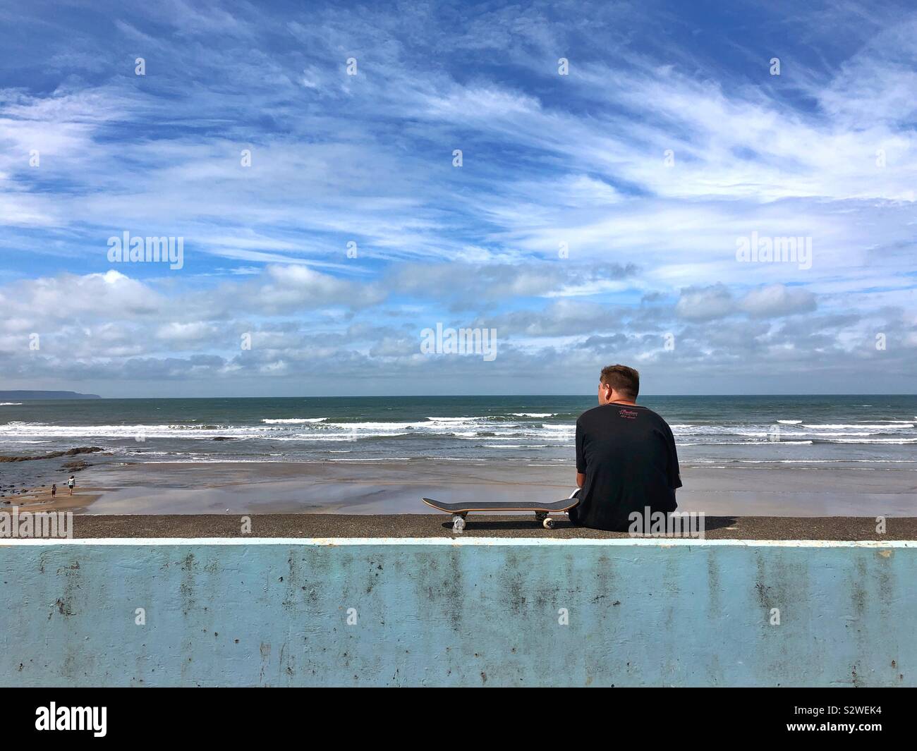 Junger Mann mit einem Skateboard beobachten Wellen am Meer. Stockfoto