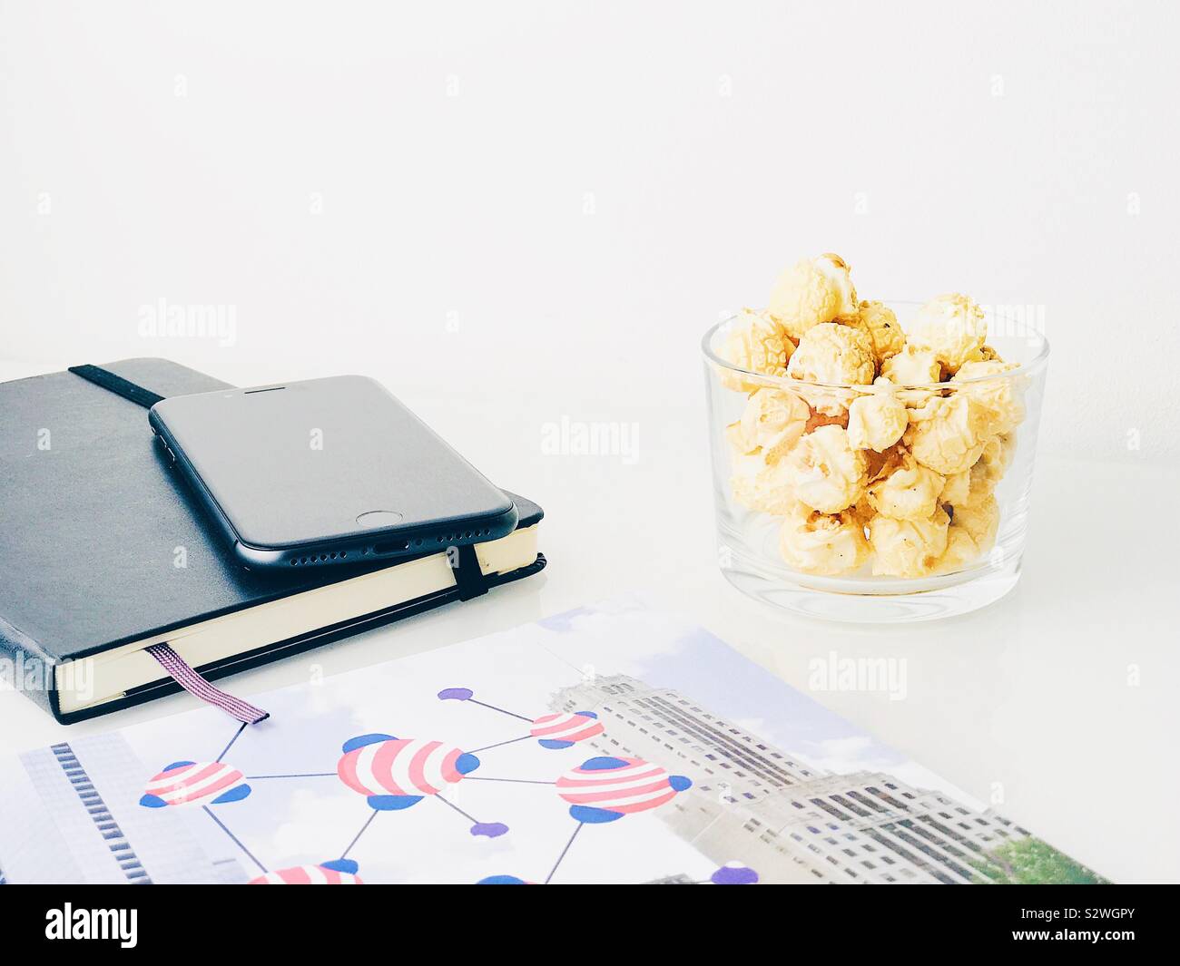 Popcorn Snack auf einem weißen oben auf ein Sideboard mit einem Notebook, Handy und ein Magazin Stockfoto