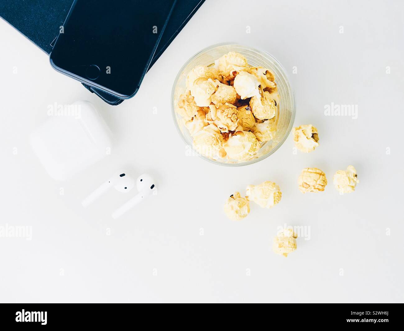 Flatlay der Weißen desk top mit Popcorn Snack, weiße Kopfhörer, Notebook und Mobiltelefon. Stockfoto