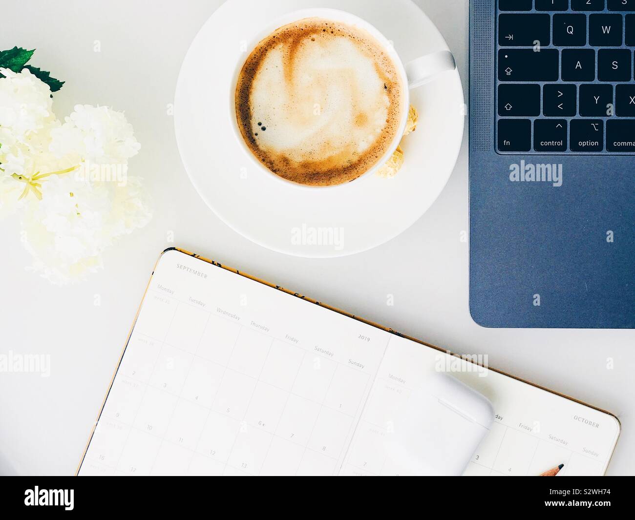 Flatlay der weißen Tisch mit Kaffee, weiße Blumen, Kopfhörer, Notebook und Laptop Stockfoto